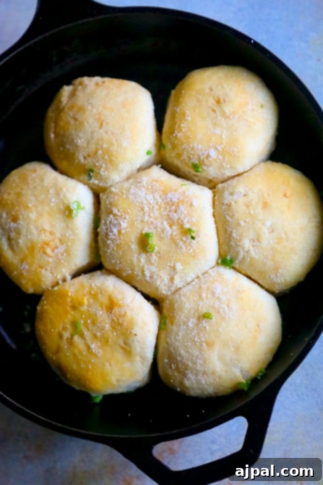 Seven golden brown garlic butter parmesan dinner rolls in a cast iron skillet, ready to be served, with a sprinkle of fresh green onions.
