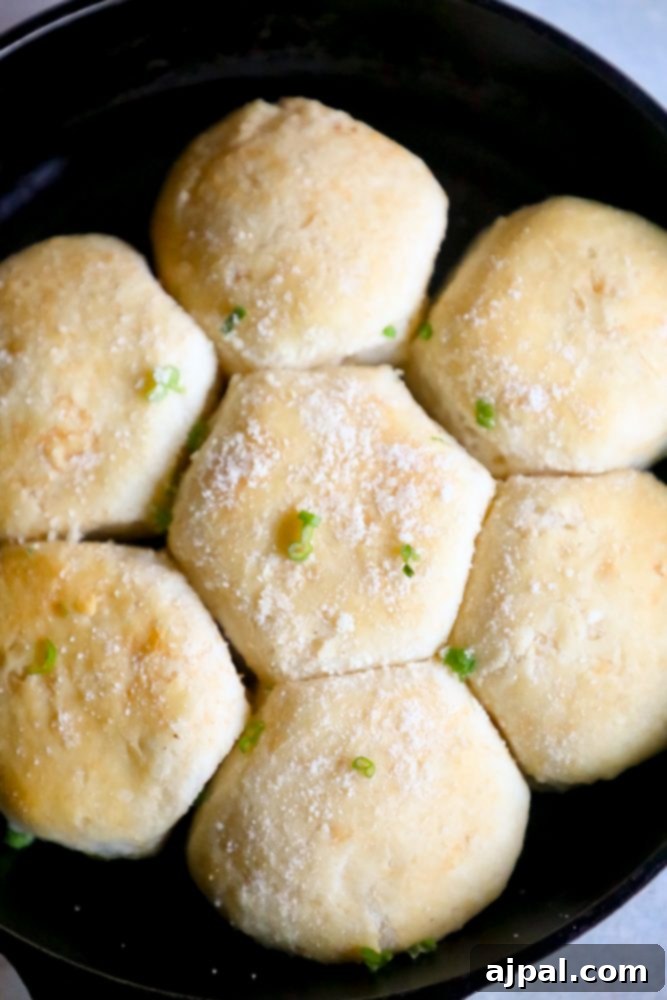A close-up of baked garlic butter parmesan dinner rolls, with melted cheese and herbs, ready to be pulled apart from the skillet.