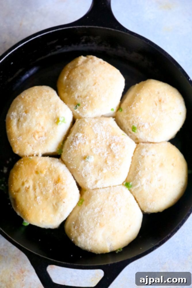 A vibrant display of garlic butter parmesan dinner rolls in a cast iron skillet, garnished with fresh green onions and ready to serve.