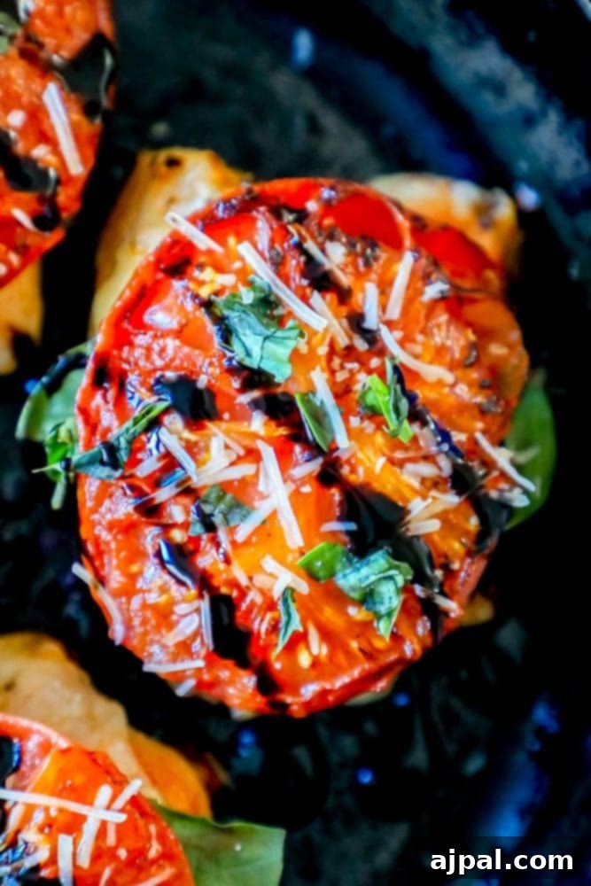Close-up of a grilled chicken thigh topped with fresh tomato, basil, melted mozzarella, and a balsamic glaze drizzle.