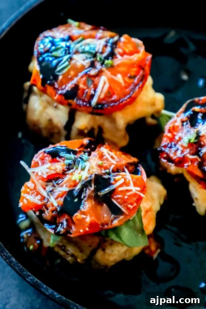 Grilled chicken thighs in a skillet, adorned with blistered tomatoes and fresh basil, ready for melted cheese.