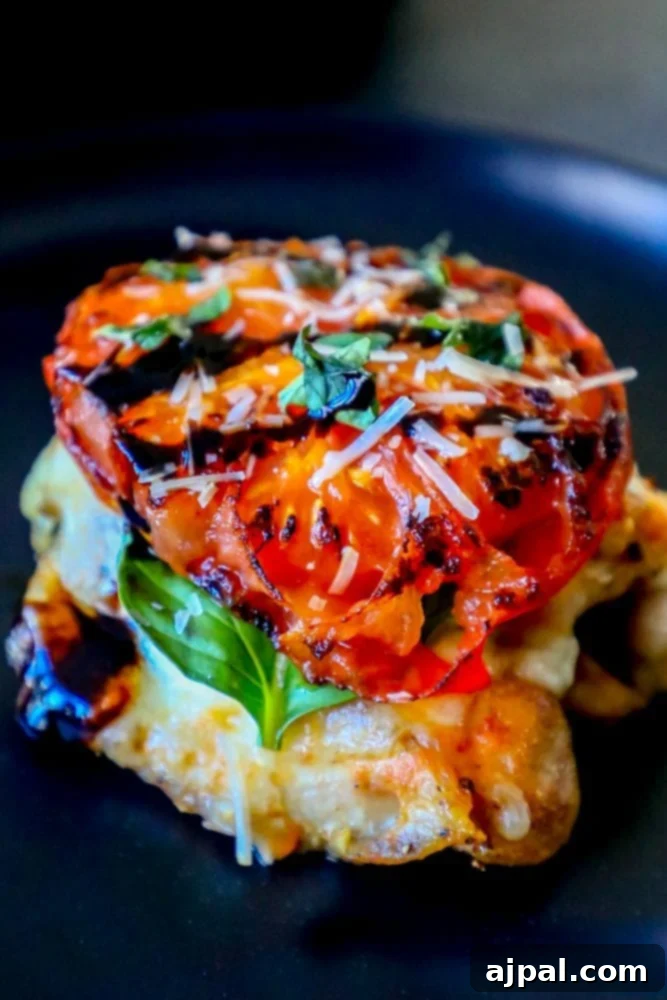 Side view of a grilled chicken thigh topped with balsamic-marinated mozzarella, roasted tomatoes, and fresh basil.