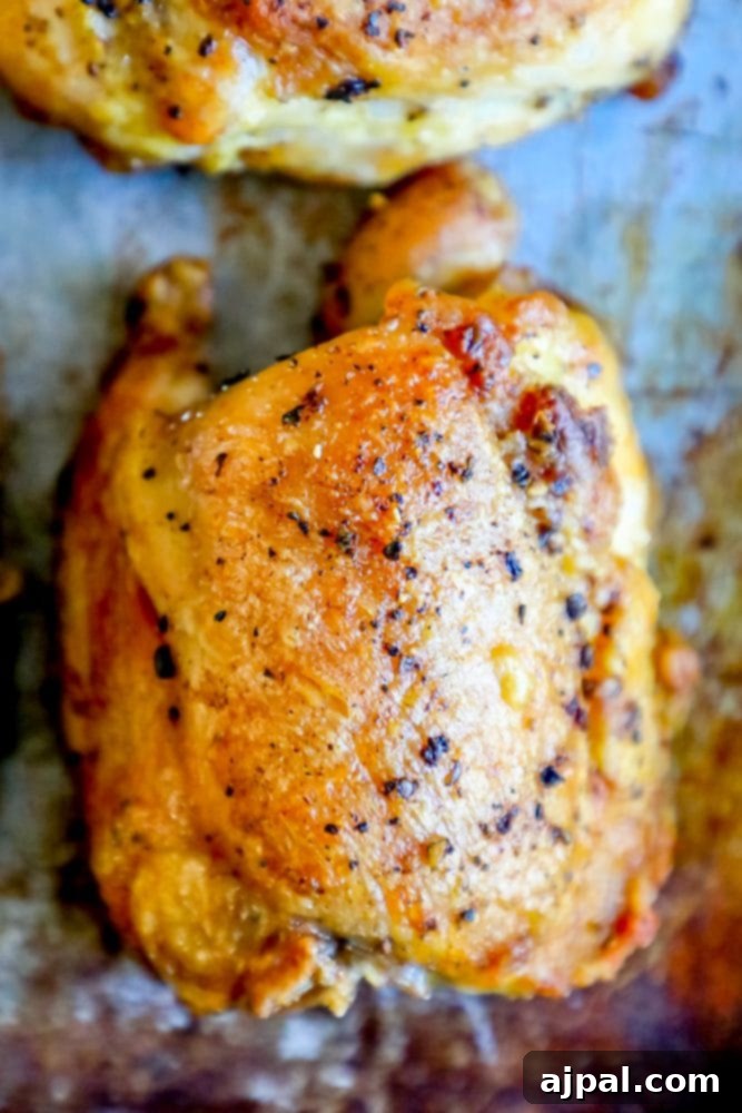 A picture of a perfectly golden-brown baked chicken thigh resting on a parchment-lined baking sheet