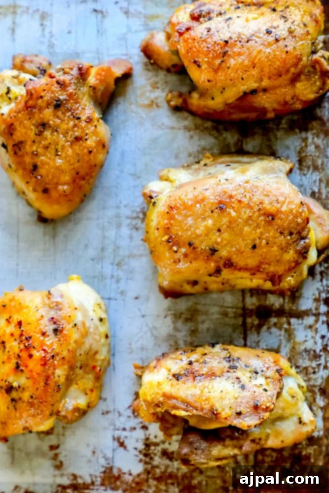 Picture of 5 baked chicken thighs on a baking sheet with cracked pepper, ready to be served