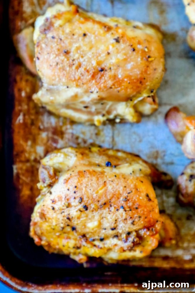 Closeup picture of two perfectly crunchy oven-baked chicken thighs on a baking sheet, glistening with savory juices