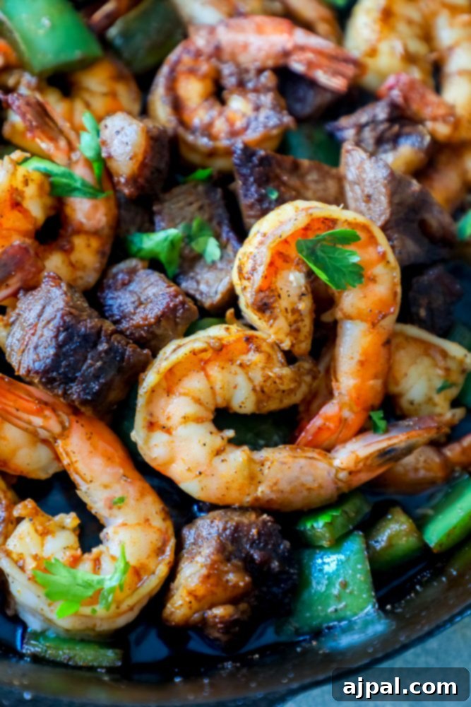Close-up of freshly cooked shrimp and steak in a skillet, garnished with green herbs.