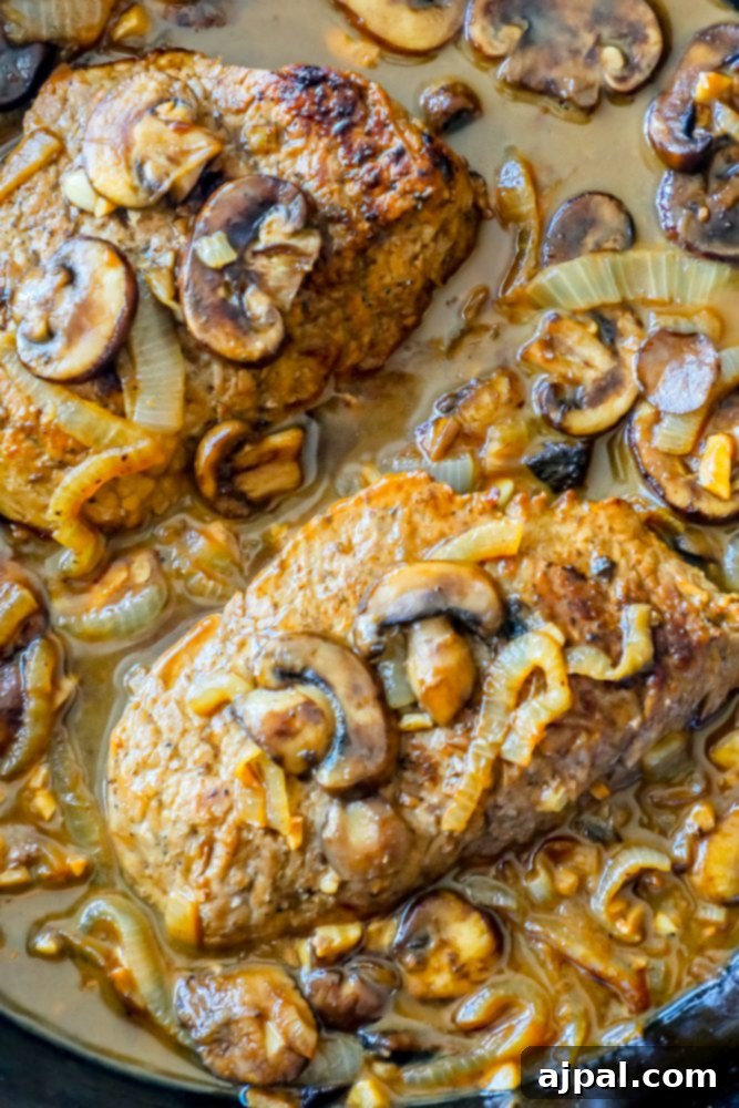 Tender Cube Steak Smothered in Savory Gravy 3 A close-up of a skillet filled with golden-brown cube steak pieces immersed in a creamy, dark mushroom and onion gravy, ready to be served.