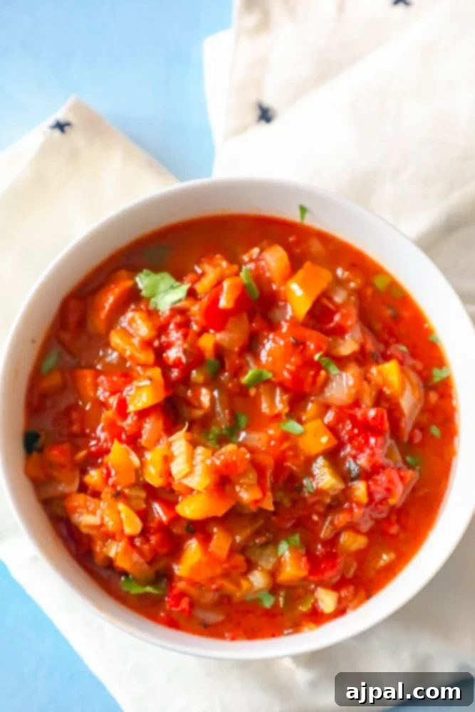 Easy Homemade Creole Sauce 4 A vibrant bowl of homemade Easy Creole Sauce, rich with tomatoes, diced onions, celery, and fresh cilantro, on a blue background.