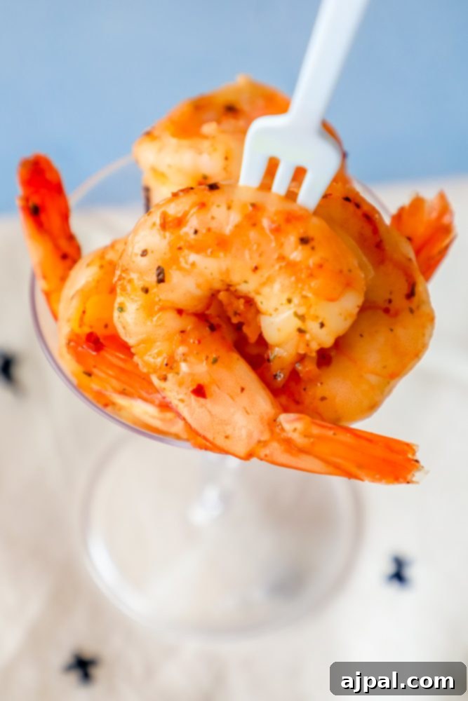 A cocktail glass brimming with succulent Cajun seasoned shrimp, ready to be enjoyed with a fork.