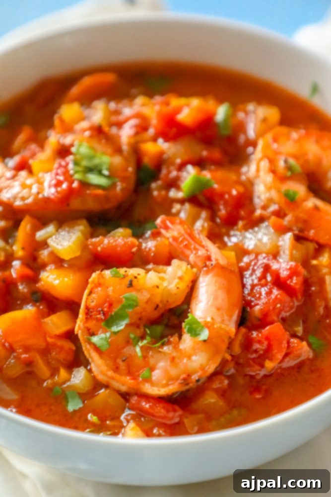 Weeknight One-Pot Creole Shrimp 4 A serving of robust Creole shrimp stew, rich with diced vegetables and tender shrimp, presented in a bowl on a dark textured surface, garnished with fresh herbs.