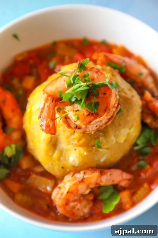 A beautifully presented bowl of Creole Shrimp Mofongo, topped with juicy shrimp and a rich red sauce, garnished with fresh herbs.