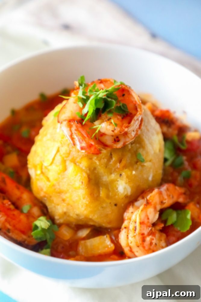A close-up of a plantain mofongo ball topped with savory shrimp in a rich, flavorful Creole sauce.