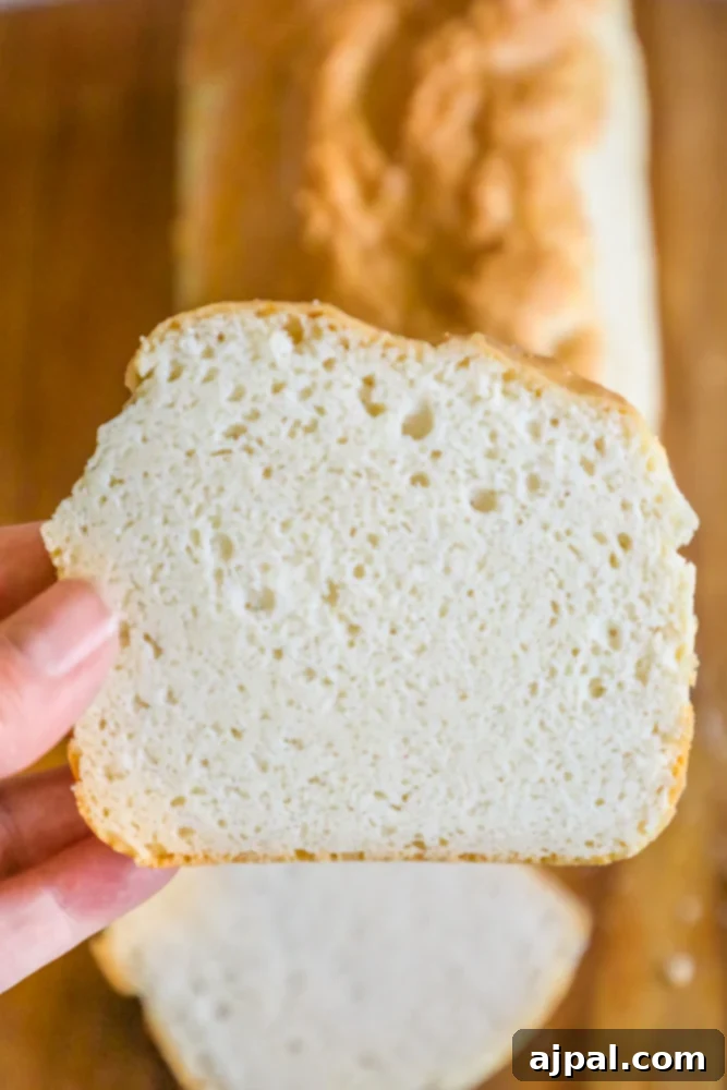 A person showcasing the Easy Keto Sandwich Bread Recipe by holding a slice of bread on a cutting board, highlighting its perfect texture.