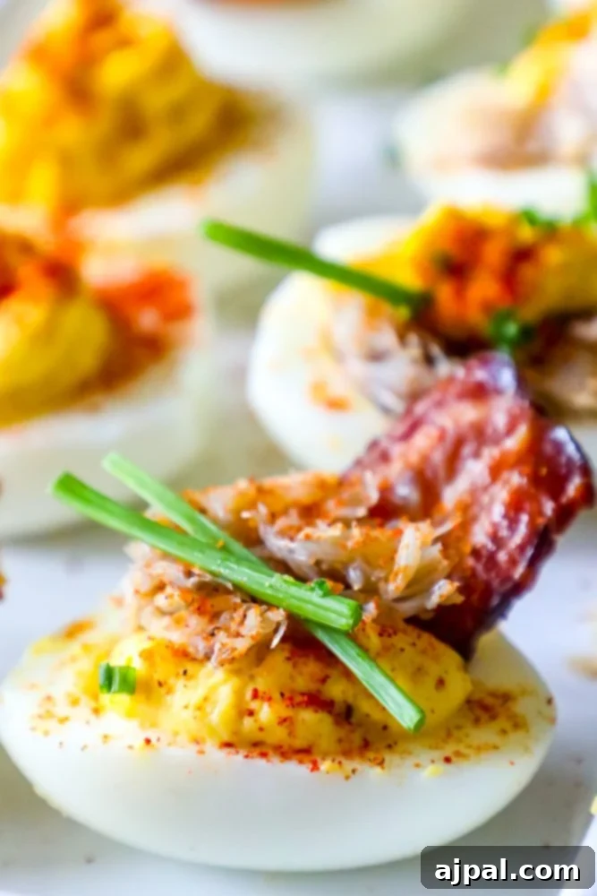 Crab and Bacon Deviled Eggs 2 Exquisitely garnished deviled egg featuring fresh chives, premium lump crab meat, and crispy bacon bits atop a creamy yolk filling, presented on a pristine white plate.