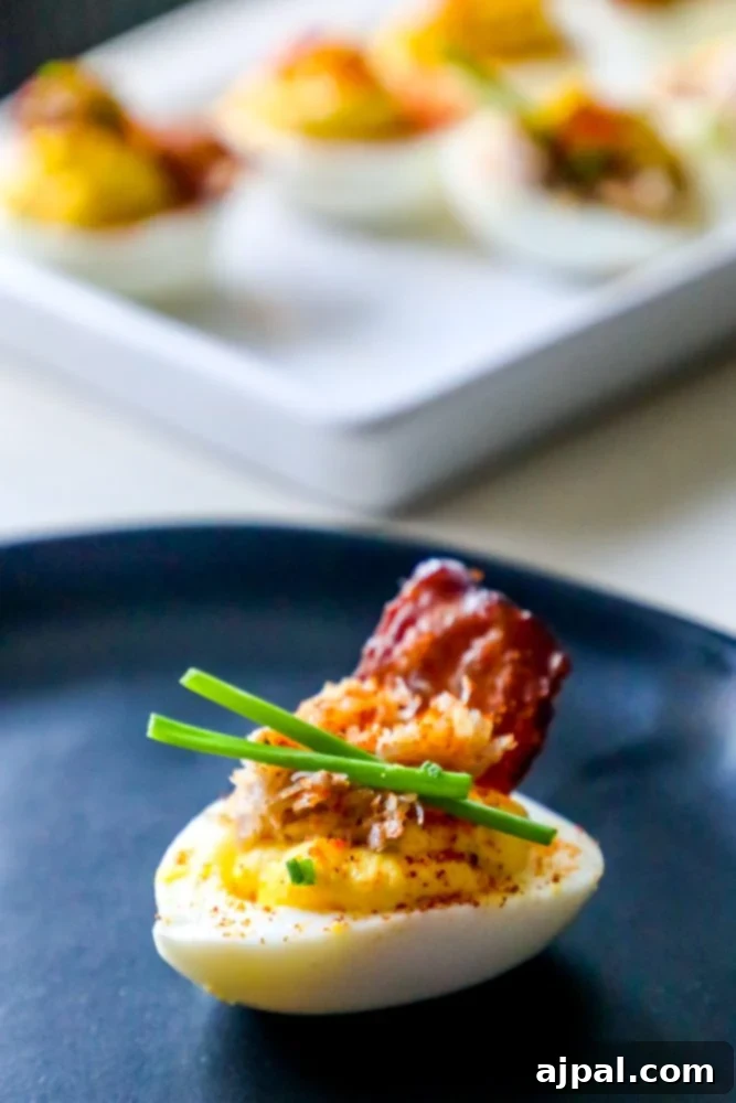 Crab and Bacon Deviled Eggs 3 A pair of beautifully arranged deviled eggs, topped with crispy bacon and fresh chives, sitting on a white background.