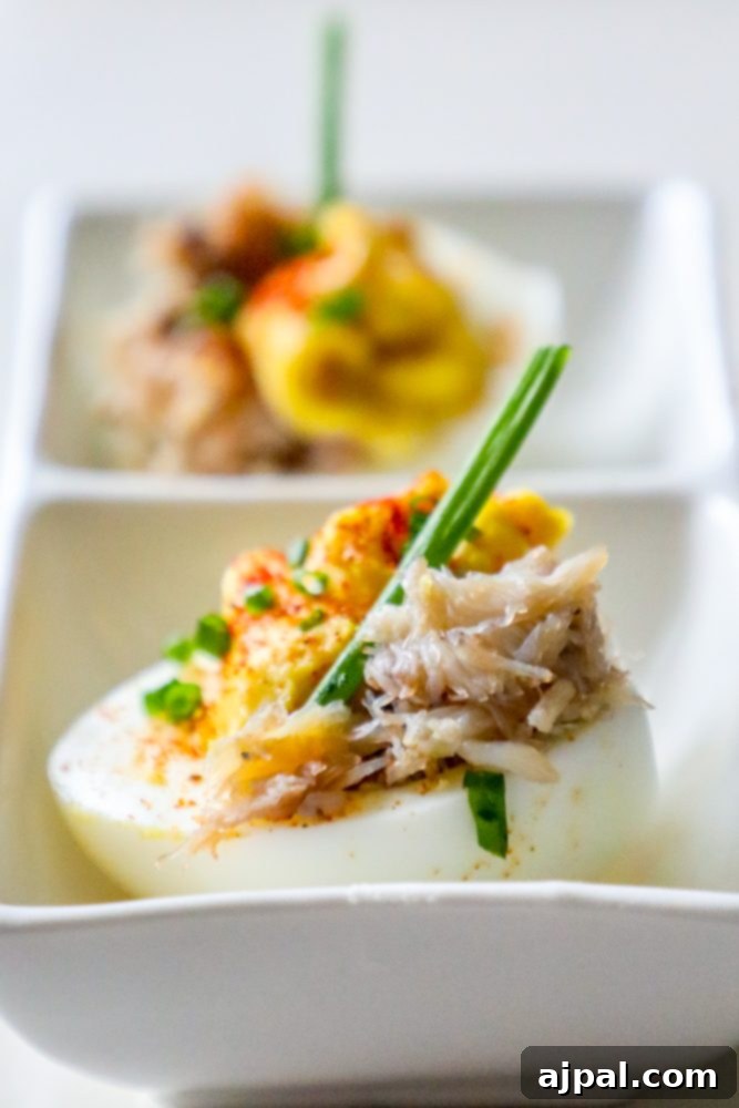Spicy Crab Bloody Mary Deviled Eggs 4 Two Keto Bloody Mary Deviled Eggs, exquisitely crafted with a creamy, spicy filling, crab meat, and a garnish of fresh herbs, presented on a white serving plate.
