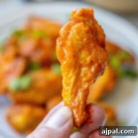 Crispy Oven Wings 11 A hand holding a single baked buffalo wing with a blurred background of more crunchy baked chicken wings on a plate.