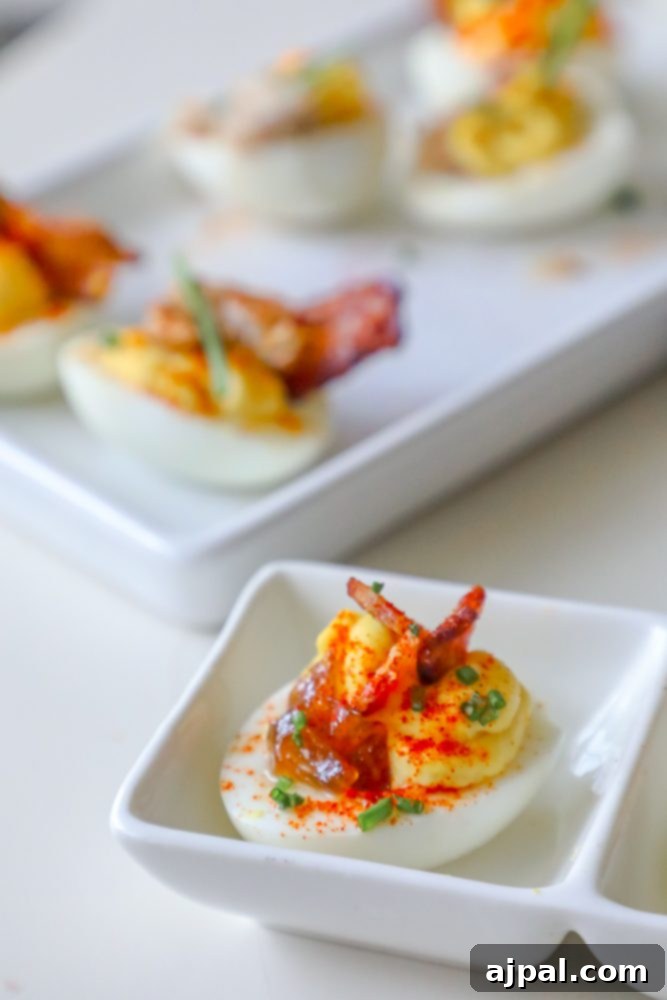 Deviled Delights with Bacon Onion Jam 3 Perfectly piped deviled eggs on a white plate, garnished with crispy bacon, fresh chives, and a dollop of sweet and savory onion jam.