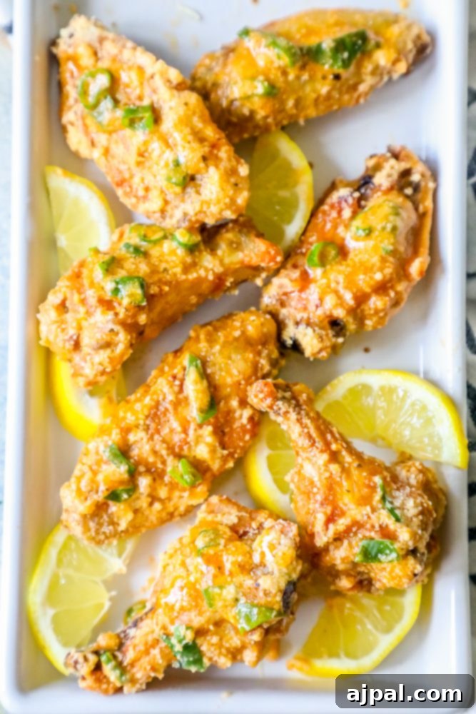 Crispy oven baked lemon garlic parmesan chicken wings served on a white plate with fresh lemon wedges.