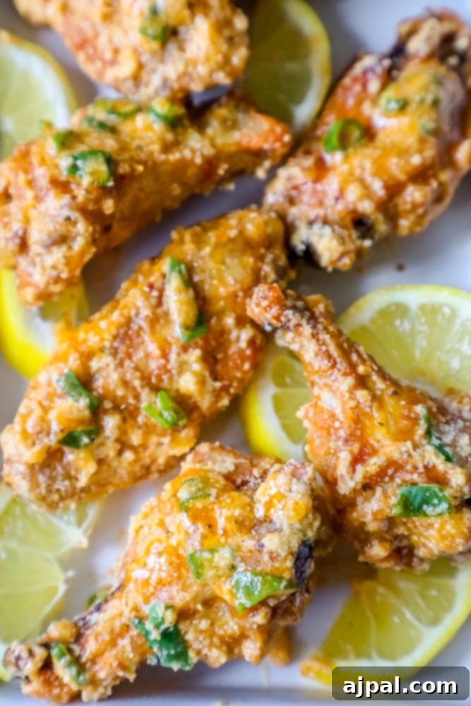 A serving of baked lemon garlic parmesan chicken wings on a white plate with lemon slices.