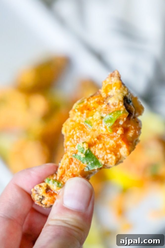 A hand holding a crispy baked lemon garlic parmesan chicken wing.