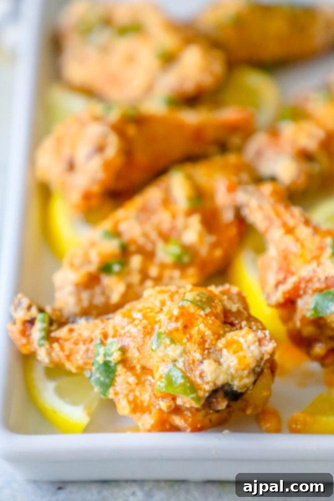 A vibrant platter of baked lemon garlic parmesan chicken wings, garnished with fresh lemon slices and herbs.