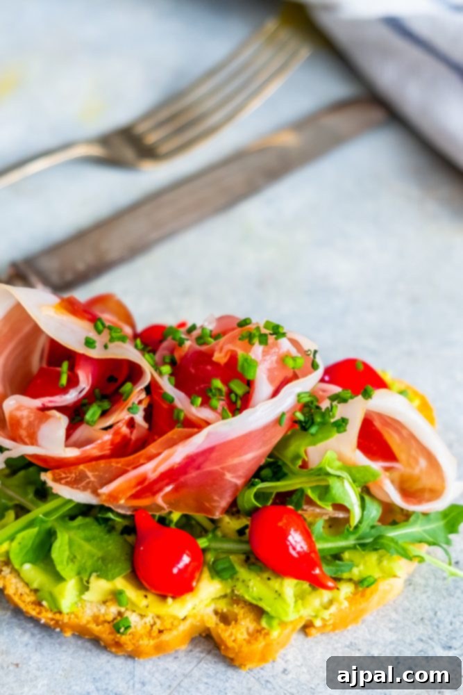 An appetizing Keto Avocado Toast adorned with fresh arugula, vibrant cherry tomatoes, and savory prosciutto, illustrating a perfect balance of flavors and textures for a low-carb diet.