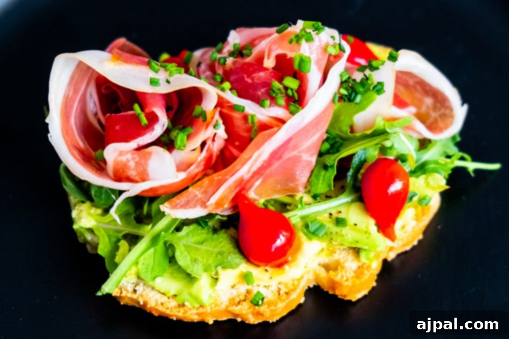 A vibrant Keto Avocado Toast on a dark plate, layered with slices of ham, fresh cherry tomatoes, and a generous smear of avocado, offering a rich and satisfying low-carb meal.