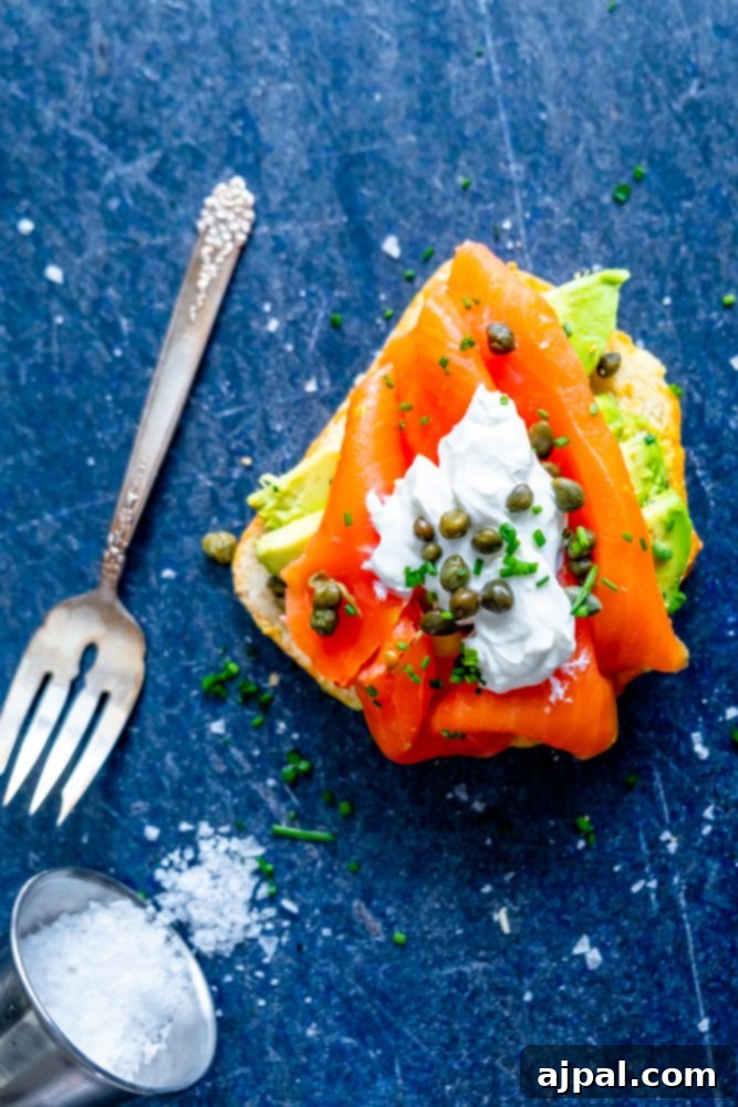 A beautifully arranged piece of toast topped with creamy avocado, smoked salmon, sour cream, capers, and fresh chives.