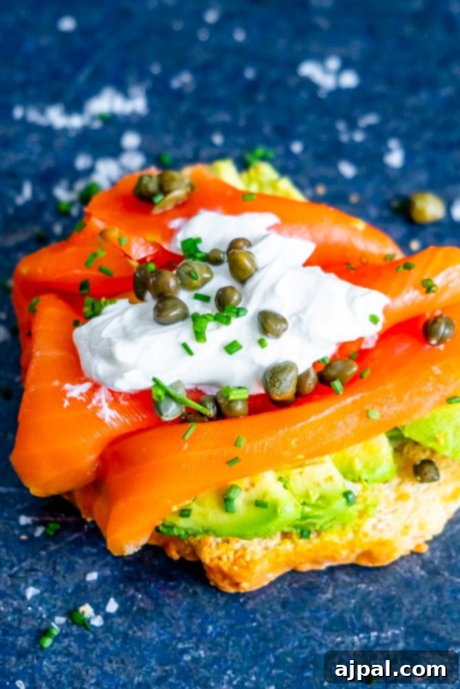 A piece of keto bread lavishly topped with avocado, smoked salmon, creamy dressing, and fresh herbs.