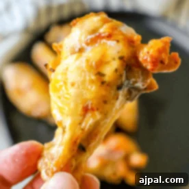 Crispy Ranch Baked Chicken Wings 7 Close-up of a hand holding a cooked chicken drumstick with crispy, golden brown skin, resembling delicious keto ranch chicken wings, over a dark plate with more drumsticks.