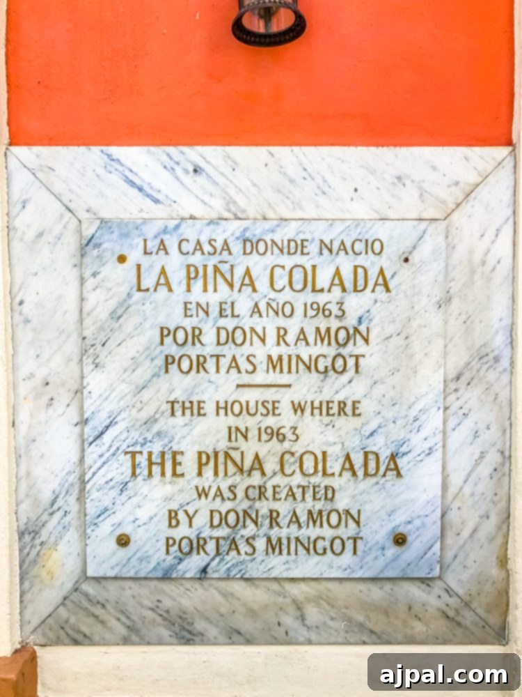 A historical plaque on a weathered wall, commemorating the invention of the Pina Colada, set against the backdrop of Old San Juan.