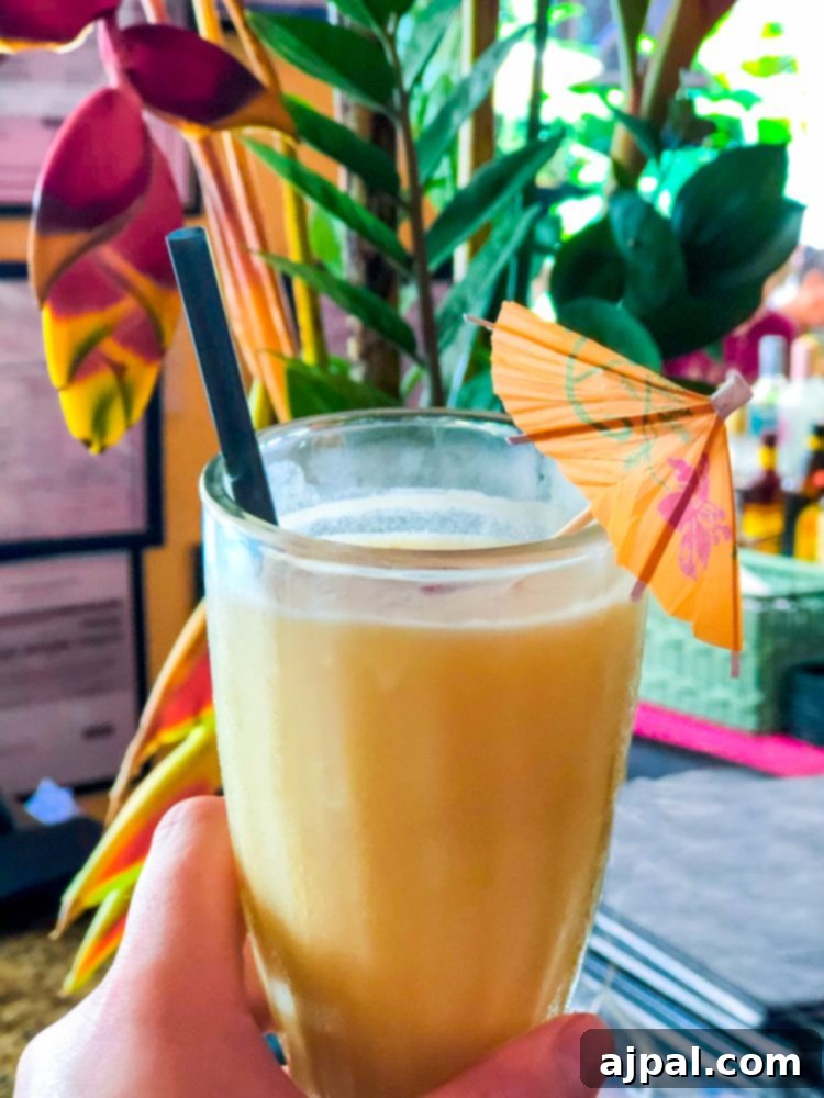 A person holding a perfectly crafted Pina Colada, garnished with a fresh palm leaf, ready to be enjoyed in a tropical setting.