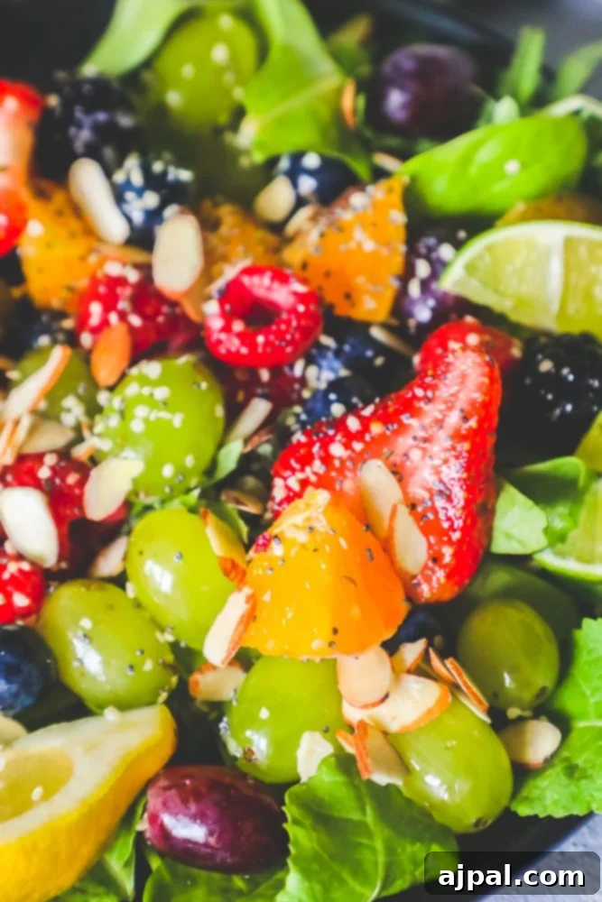 A vibrant fruit salad featuring spinach, grapes, oranges, lemon slices, almonds, poppyseeds, and strawberries, served in a large bowl.