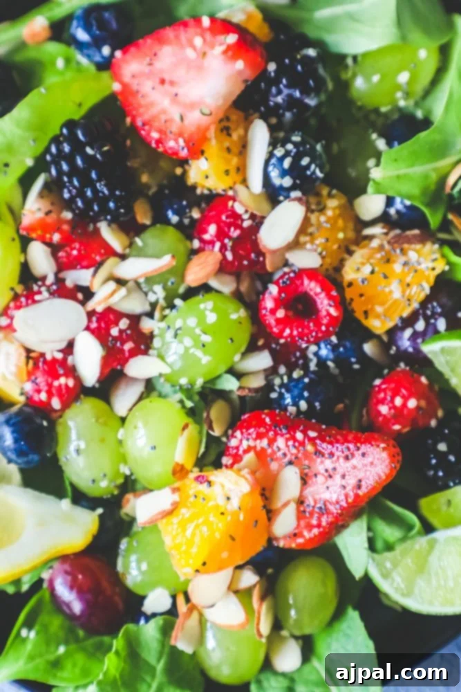 A close-up shot of a Poppyseed Spinach Fruit Salad, showcasing fresh spinach leaves, mixed berries, orange slices, and a generous sprinkle of poppy seeds and almonds.