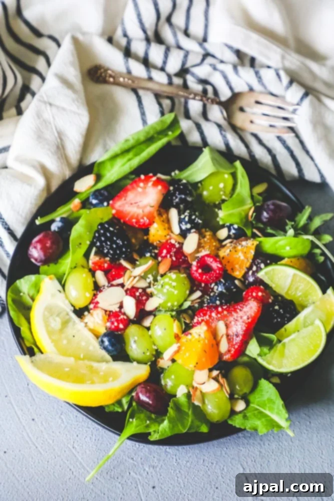 A beautifully composed fruit salad in a large glass bowl, garnished with lemon slices, almonds, and a drizzle of poppyseed dressing, highlighting the fresh ingredients.