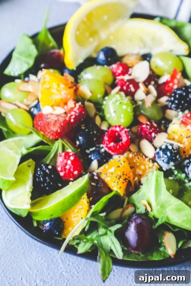 A bowl of refreshing fruit salad with spinach, oranges, grapes, and strawberries, topped with poppyseeds, ready to be served.