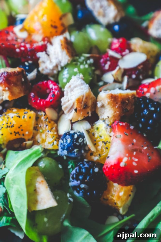 Close-up of a perfect chicken and fruit salad with poppyseed dressing, showcasing vibrant berries, crisp spinach, and tender chicken cubes against a contrasting black plate.