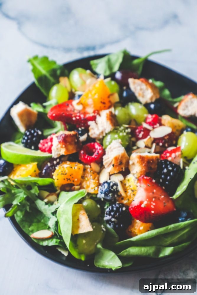 A close-up shot of a chicken and fruit salad with poppyseed dressing on a black plate, showcasing the colorful array of ingredients and the rich texture of the dressing.