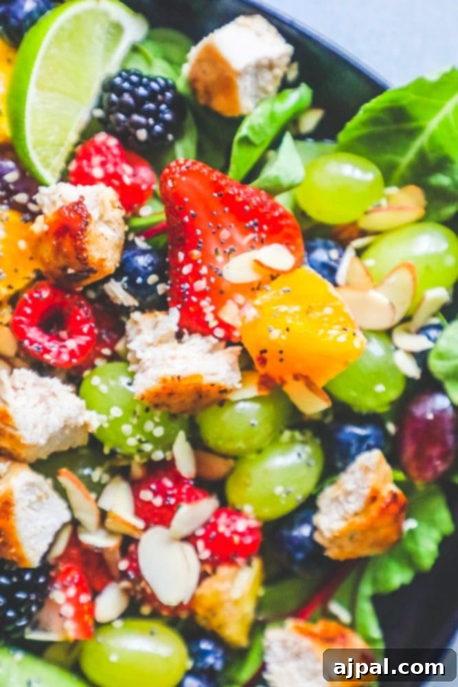 A vibrant and refreshing chicken salad with various fruits and a generous drizzle of citrus poppyseed dressing, presented on a black plate.