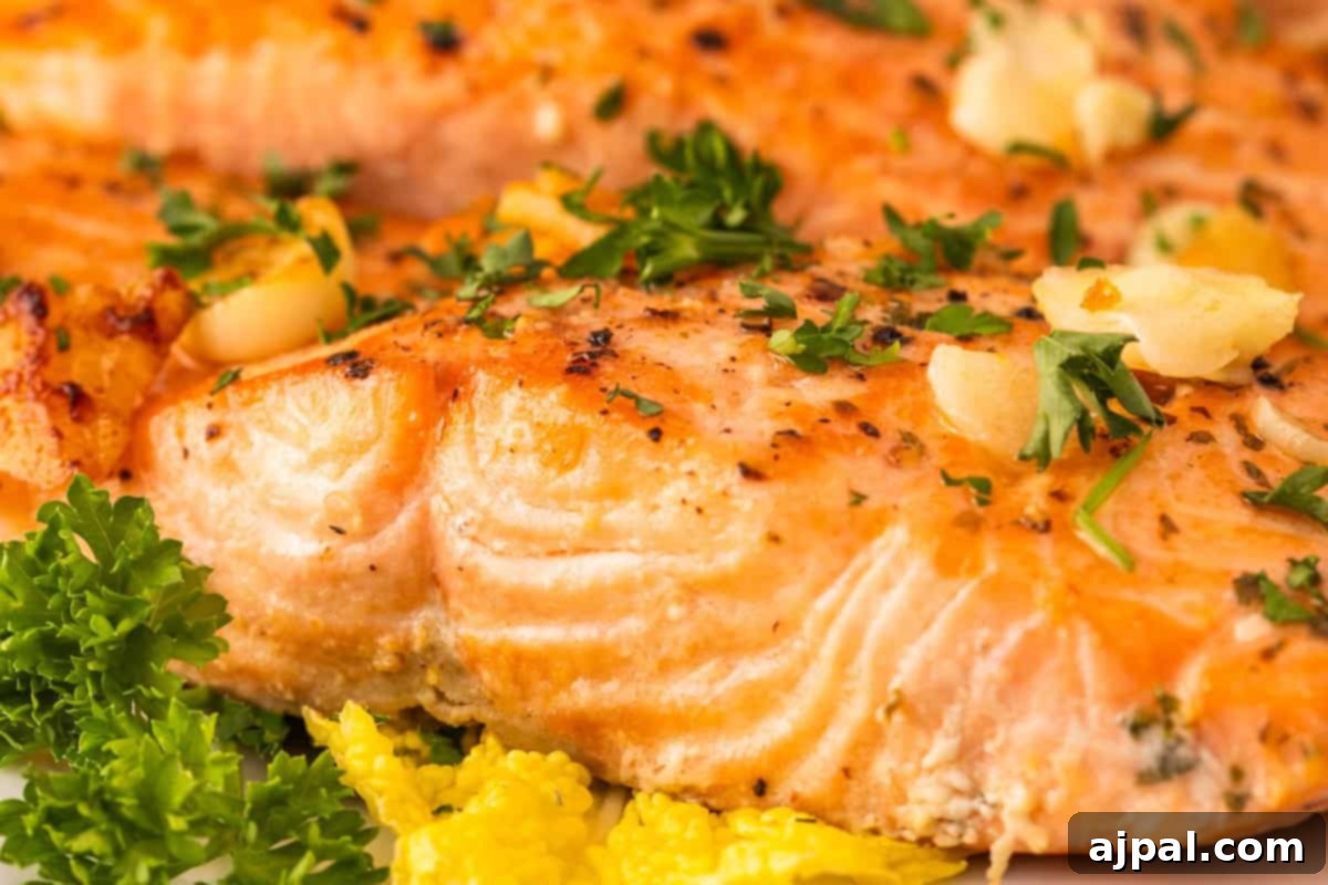 Effortless Oven-Baked Salmon 2 Close-up of garlic baked salmon recipe: a cooked salmon fillet garnished with parsley and garlic, accompanied by yellow vegetables and fresh parsley.