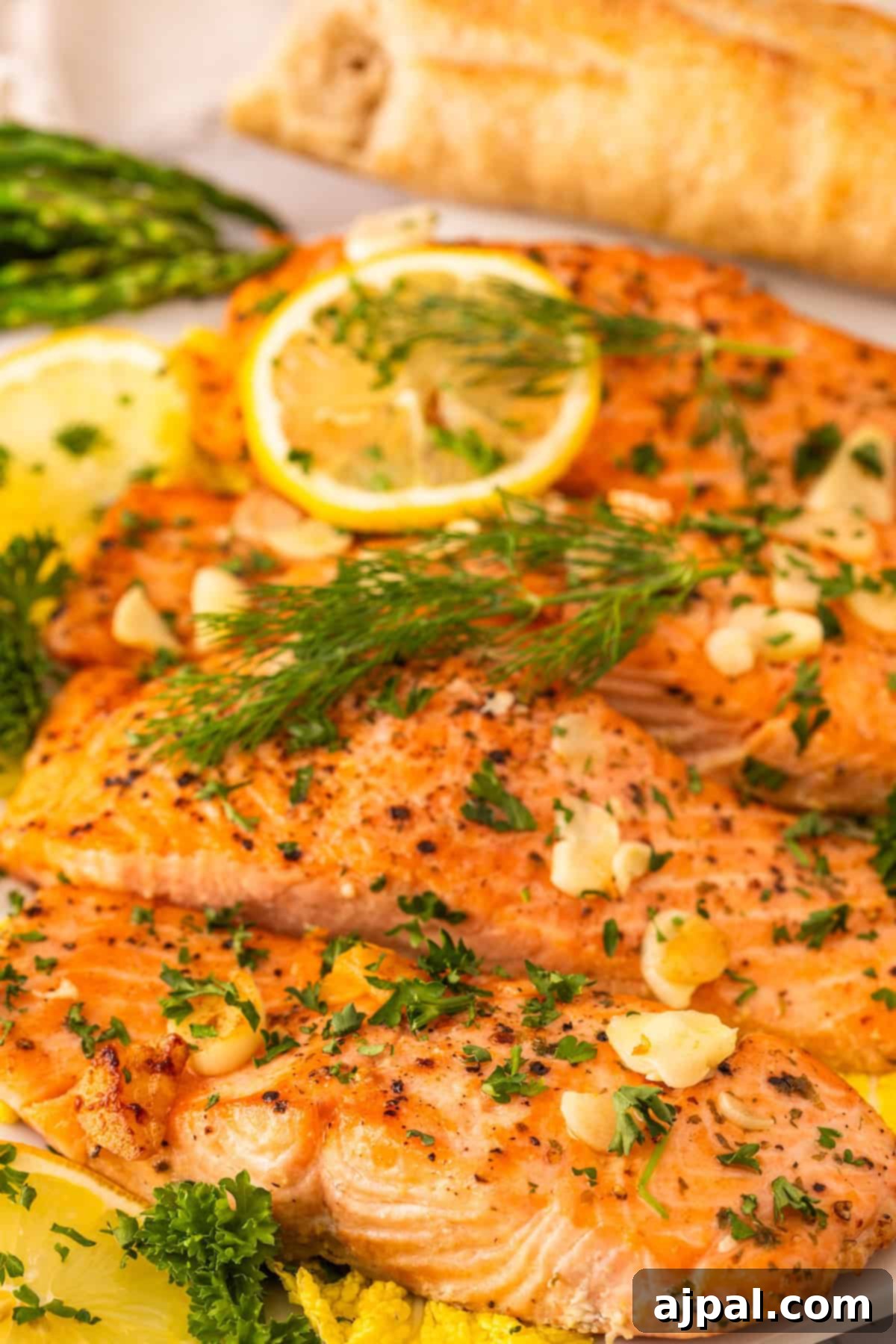 Effortless Oven-Baked Salmon 8 Grilled salmon fillets garnished with fresh dill, parsley, garlic, and lemon slices—this dish rivals the Best Baked Salmon recipe—served with asparagus and bread in the background.