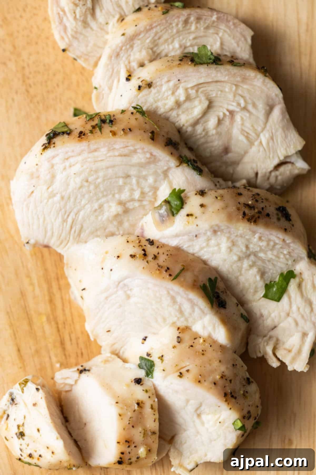 Sliced, easy baked chicken breast seasoned with herbs and black pepper on a wooden cutting board.