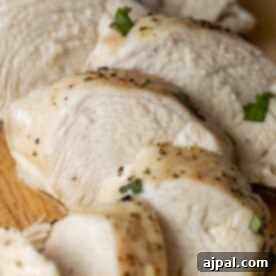 Sliced cooked chicken breast on a wooden cutting board, seasoned with herbs and black pepper. The Best Easy Baked Chicken Breasts Recipe ensures juicy and flavorful chicken every time.