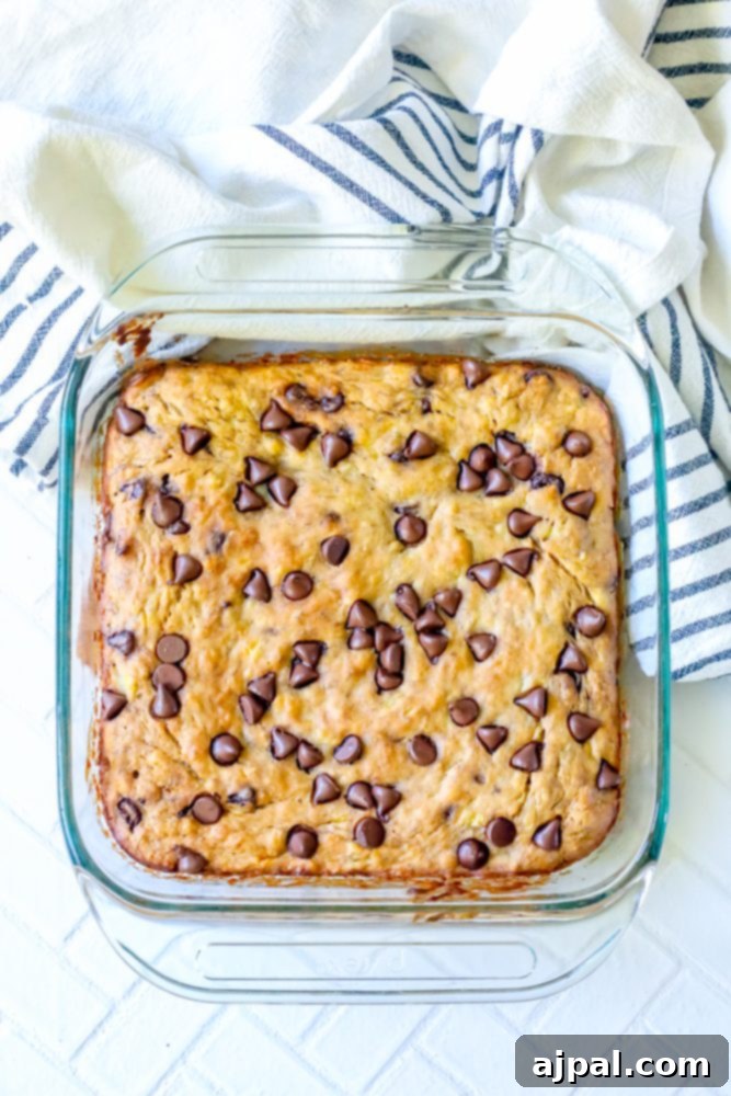A rectangular glass baking dish filled with golden-brown banana chocolate chip bars, one piece artfully removed to show its soft interior.
