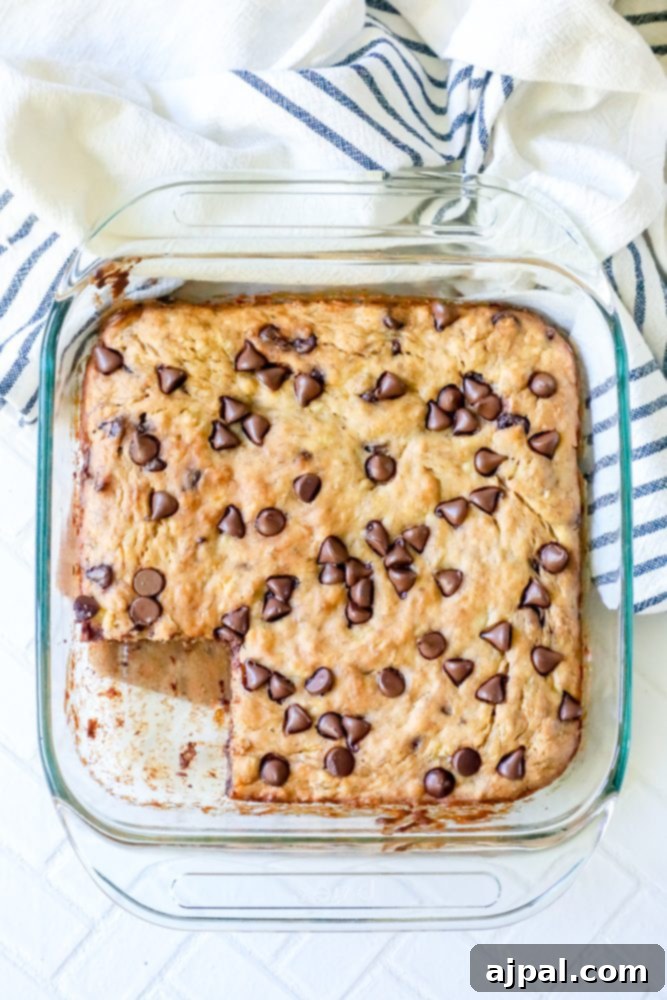 A glass baking dish containing freshly baked banana chocolate chip bars, with one square piece already missing, highlighting their tempting appeal.