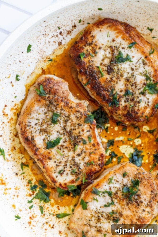 Perfectly Pan Fried Thin Pork Chops 2 A perfectly pan-fried pork chop, golden brown and garnished with fresh herbs, resting in a hot skillet.