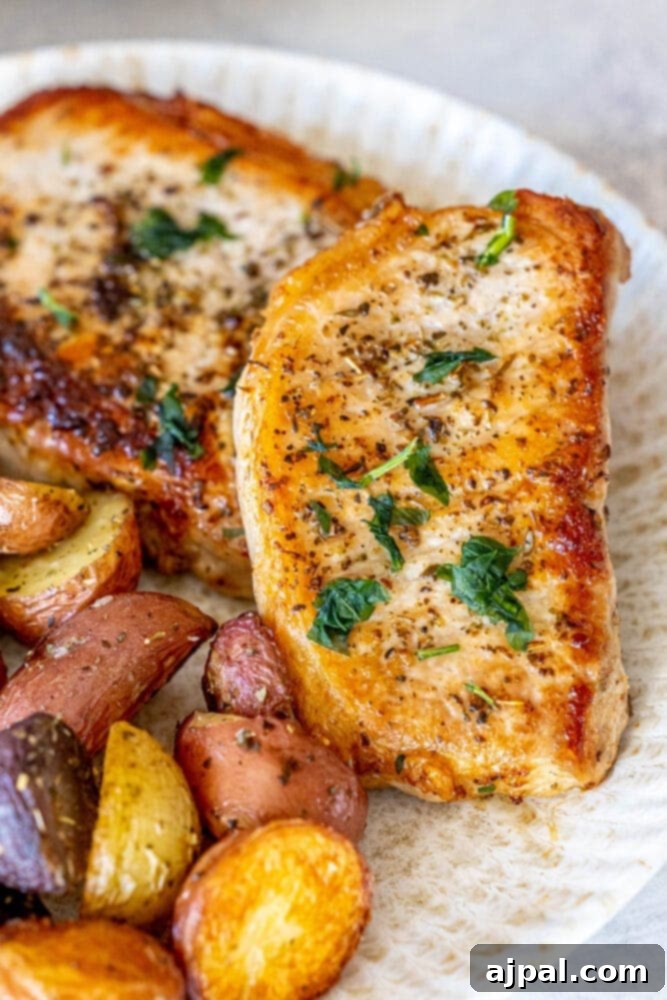 Perfectly Pan Fried Thin Pork Chops 11 A beautifully plated dinner featuring pan-fried pork chops served alongside roasted potatoes, garnished with fresh herbs.