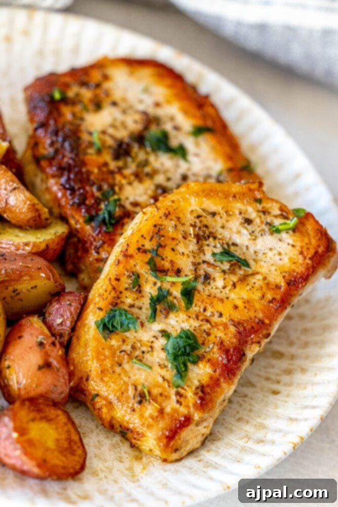 Perfectly Pan Fried Thin Pork Chops 12 A delectable meal of golden pan-fried pork chops and roasted potatoes, perfectly arranged on a white plate with fresh parsley garnish.