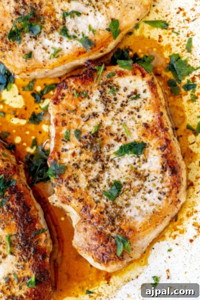 Perfectly Pan Fried Thin Pork Chops 4 Three golden-brown pan-fried pork chops sizzle invitingly in a cast iron skillet, ready to be served.